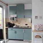 Küche mit blauen Schränken, Mikrowelle und Fenster zum Balkon.