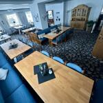 Großer Raum mit mehreren Tischen und blauen Sofas auf gemustertem Teppich.