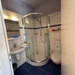 Badezimmer mit Dusche, Waschbecken und Toilette. Fliesenboden und Wandfliesen.