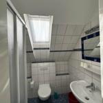 Badezimmer mit Toilette, Waschbecken und Dusche unter Dachschrägen.