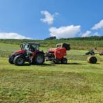 Ein roter Traktor bindet Heu in einem grünen Feld.