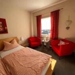 Ein Schlafzimmer mit Bett, zwei roten Sesseln und Fenster mit roten Vorhängen.