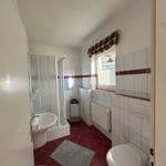 Badezimmer mit Dusche, Waschbecken und Toilette. Rote Fliesen und Fenster mit Vorhang.