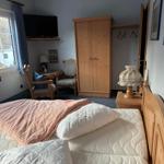 Schlafzimmer mit Bett, Kleiderschrank und Fernseher an der Wand.