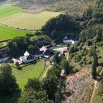 Aerial view of a rural property with houses, green fields, and dense forest.