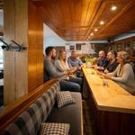 Gruppe sitzt an Holzbar mit Sitzbank und Kissen.