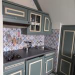 Küche mit grünen Schränken, Fliesenwand und Edelstahlspüle.