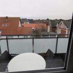 Balcony with table and chairs overlooking rooftops and snowy ground.