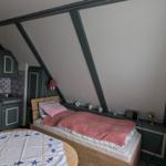 Ein Schlafzimmer mit kleiner Küche und Tisch. Holzbett mit rosa Bettwäsche.