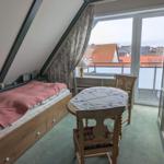 Schlafzimmer mit Dachschräge, Bett, Tisch und Balkonblick.
