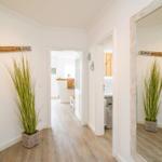 Flur mit Holzboden, großer Pflanze und Spiegel. Wanddekoration mit Schild.