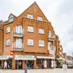 Zweistöckiges Gebäude mit Geschäften im Erdgeschoss und Balkonen an den Fenstern.