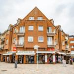 Zweistöckiges Backsteinhaus mit Geschäften im Erdgeschoss und Balkonen an den Fenstern.