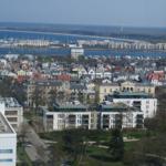 Stadtansicht mit Häusern, Park und Hafen mit Booten.