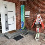 Eingang mit rotem Backsteinhaus, Briefkasten und buntem Holzhaus.