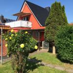 Rotes Haus mit Balkon, Solaranlage und Garten mit Rosen.