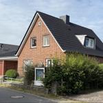 Rotes Backsteinhaus mit schwarzem Dach und grüner Hecke