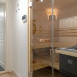 Sauna mit Holzbank und Glaswand. Nebenraum mit Dusche und Handtuchhalter.