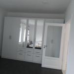 Schlafzimmer mit weißem Schrank und Spiegeltüren, dunkler Bodenfliese und Tür zum Anschlussraum.