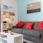 Ein Wohnzimmer mit grauem Sofa, roten Kissen und zwei Wandbildern an den Wänden.