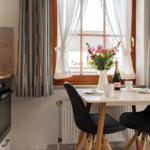 Essbereich mit Tisch, Stühlen und Fenster mit Blumen und Flasche.