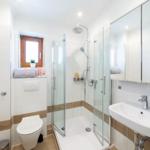 Badezimmer mit Dusche, Waschbecken und Toilette. Holzakzent an Wänden.