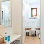 Badezimmer mit Dusche, Toilette und Spiegel. Auf Ablagefläche stehen Flasche und Dose.