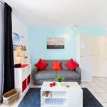Wohnzimmer mit grauem Sofa, roten Kissen und weißem Couchtisch.