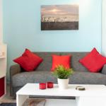Ein Wohnzimmer mit grauem Sofa, roten Kissen und weißem Couchtisch.