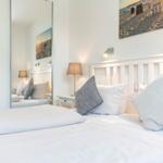 Schlafzimmer mit weißem Bett, Wandspiegel und Wandbild.