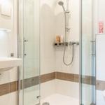 Badezimmer mit Dusche, Waschbecken und Toilette. Holzakzentstreifen an den Wänden.