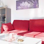 Rotes Sofa, weißer Tisch, Wandbild mit Lotus, Bücherregal und Tür im Hintergrund.