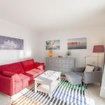 Wohnzimmer mit rotem Sofa, grauer Sitzgruppe und buntem Teppich.