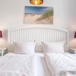 Schlafzimmer mit weißem Bett, zwei Nachttischen und einer Strandbilddekoration.