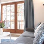 Ein Wohnzimmer mit Sofa, Tisch und Blumen vor Fenster mit Blick auf Balkon.