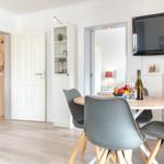 Essbereich mit runder Tisch, grauen Stühlen und Fernseher an der Wand.