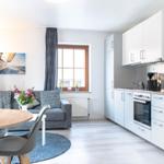 Wohnküche mit grauem Sofa, Essplatz und Küchenzeile.