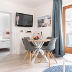 Wohnraum mit Esstisch, TV und Blick auf Balkon. Schlafzimmer im Hintergrund.
