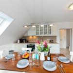 Esszimmer mit Holztisch, weißen Stühlen und Küchenbereich unter Dachschrägen.