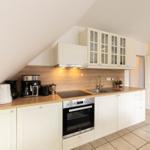 Küche mit weißen Schränken, Holzoberfläche und integriertem Backofen unter schrägem Dach.