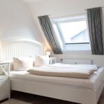 Schlafzimmer mit Dachfenster, weißem Bett und Holzboden.