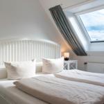 Schlafzimmer mit Dachschrägen, Dachfenster und weißem Bett.