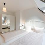 Schlafzimmer mit Dachschrägen, weißem Bett und Spiegelschrank.