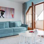 Ein Wohnzimmer mit blauem Sofa, weißen Tischen und einer großen Fensterfront.