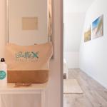 Flur mit Wandbildern und Tür. Auf Tisch: Tasche und Wasserflasche.