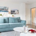 Wohnzimmer mit hellblauem Sofa, weißen Wänden und Segelyachten-Bildern an der Wand.