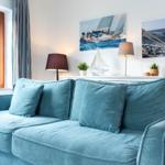 Blauer Sofa mit Kissen, Wandbilder von Segelbooten und Fenster mit Holzrahmen.