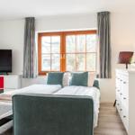 Schlafzimmer mit Bett, TV und Fenster. Möbel sind weiß und grün.