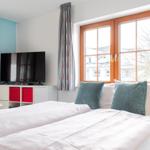 Zimmer mit Doppelbett, TV und Fenster mit Blick auf Gebäude.