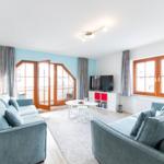 Wohnzimmer mit zwei Sofas, TV und Balkontür. Fenster mit Holzrahmen.